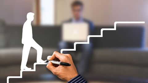 Karriereleiter Eine Person, die eine Treppe hinaufsteigt, wird auf eine Glasscheibe gemalt. Im Hintergrund eine Person mit Notebook